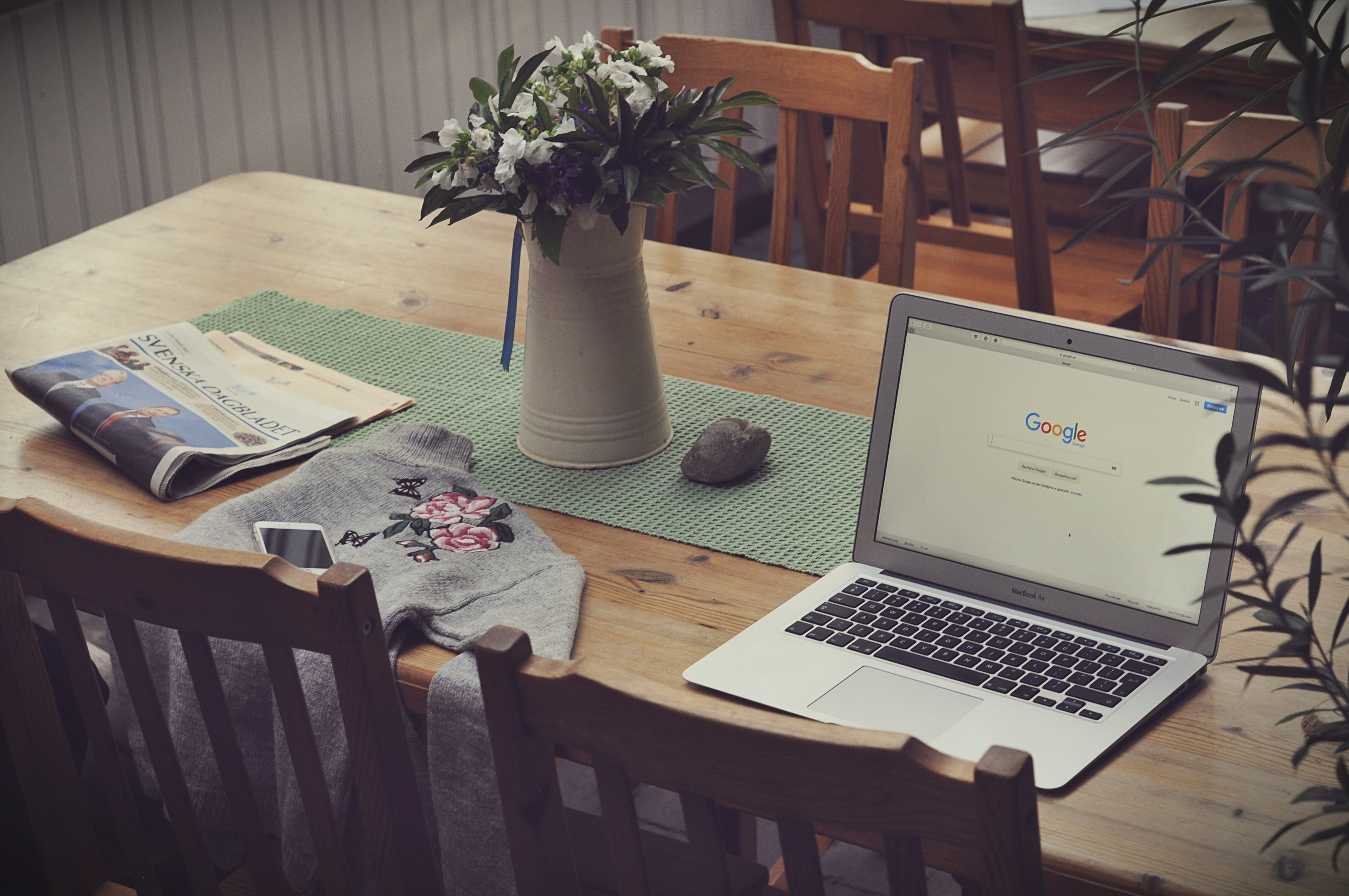 Work from home workspace: laptop, newspaper, phone, and jacket laid on kitchen table
