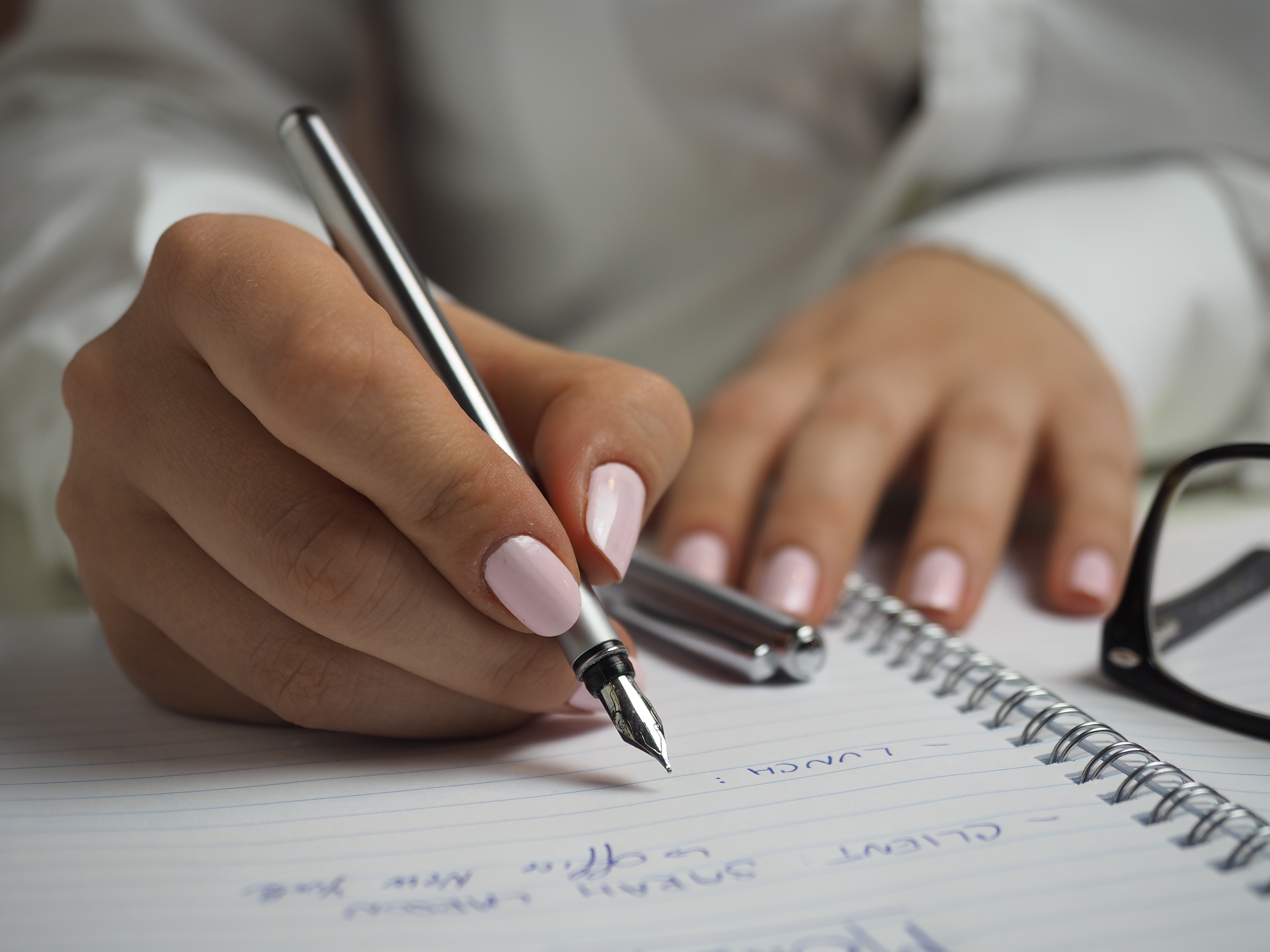 Hand with painted nails writing in planner with glass to the side