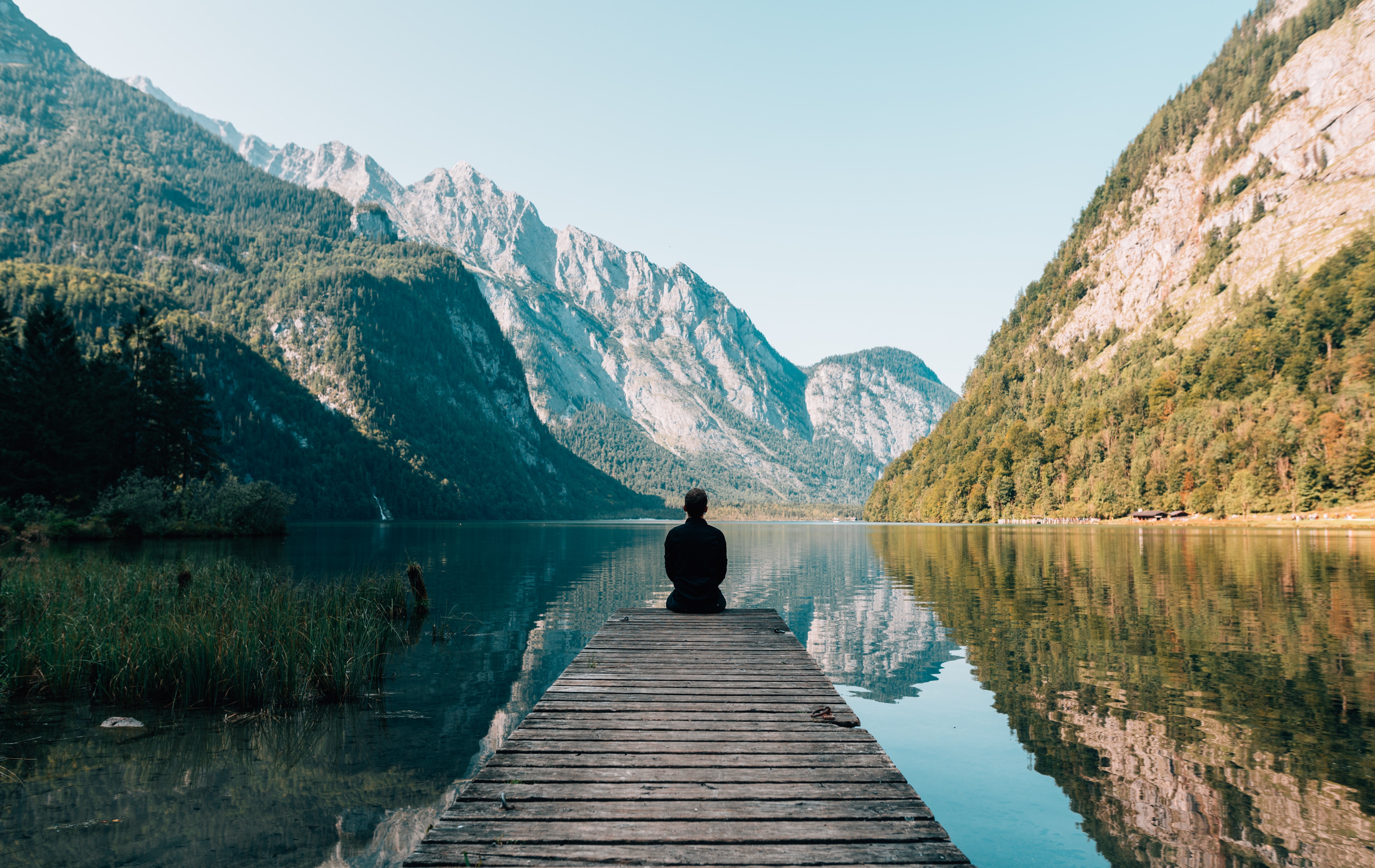 Person sits on end of dock surrounded by mountains