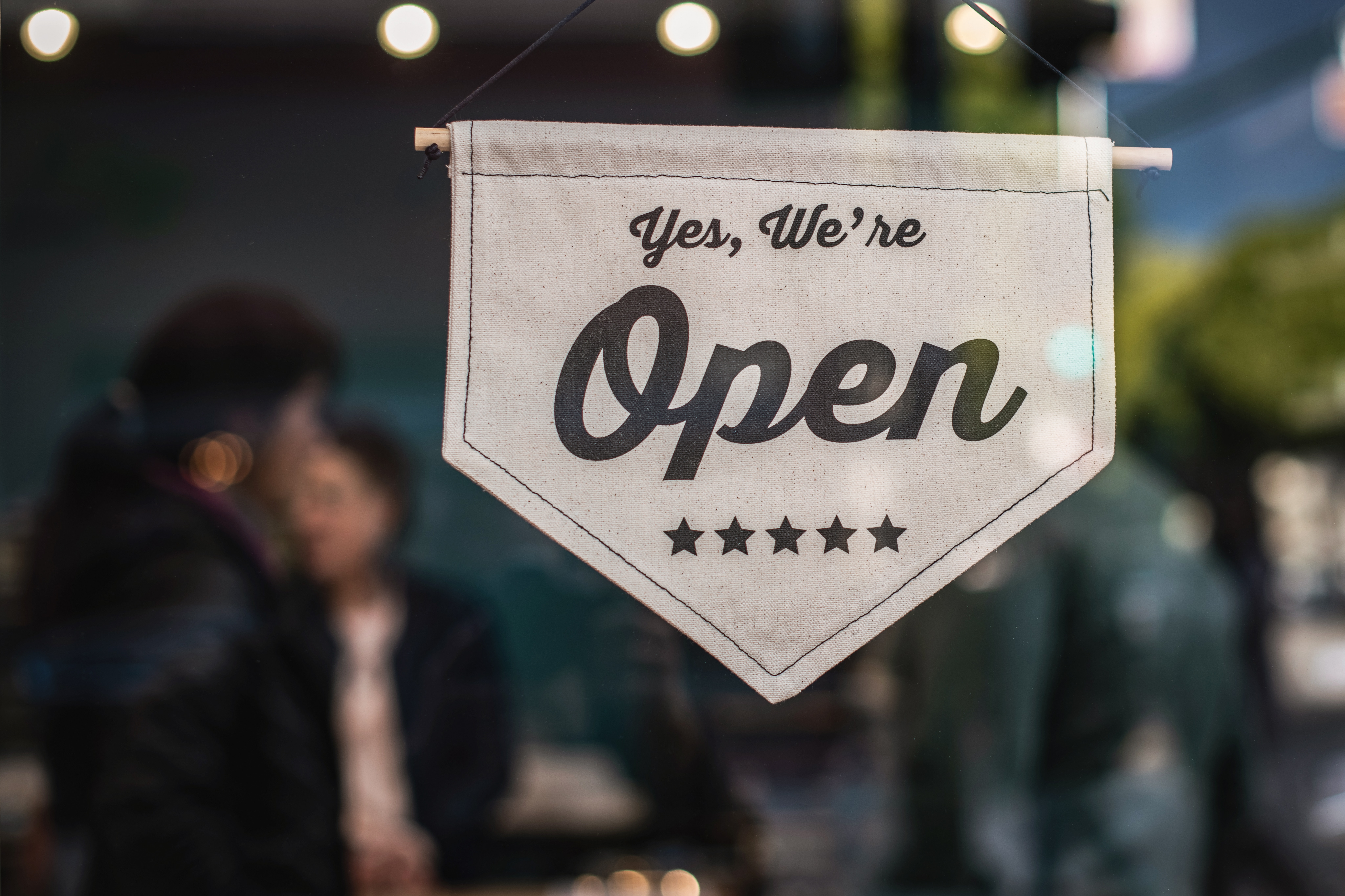 Store window with shallow focus on flag that says, "Yes, we're open."