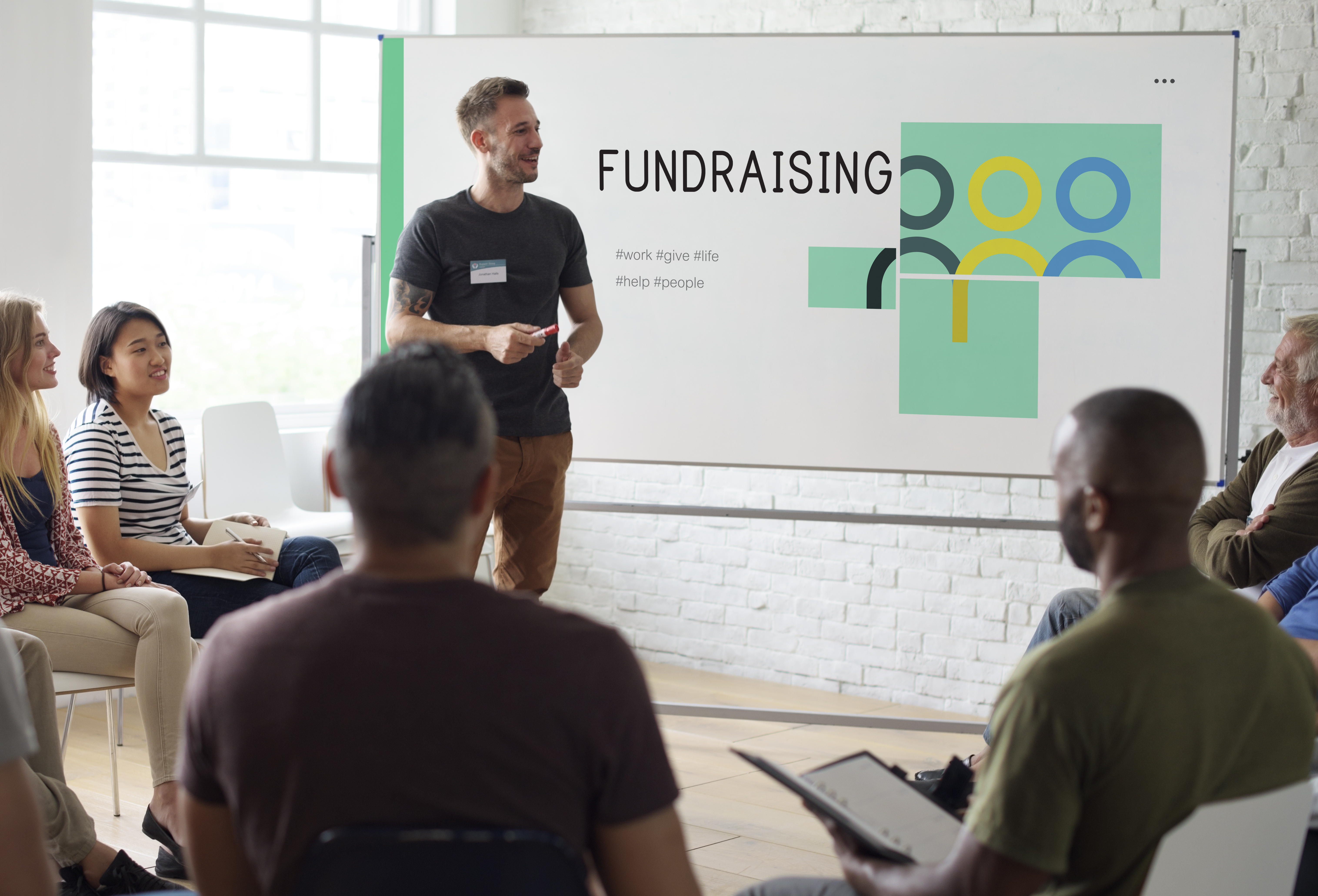 Man presents to group of people while standing in front of a board saying "Fundraising"