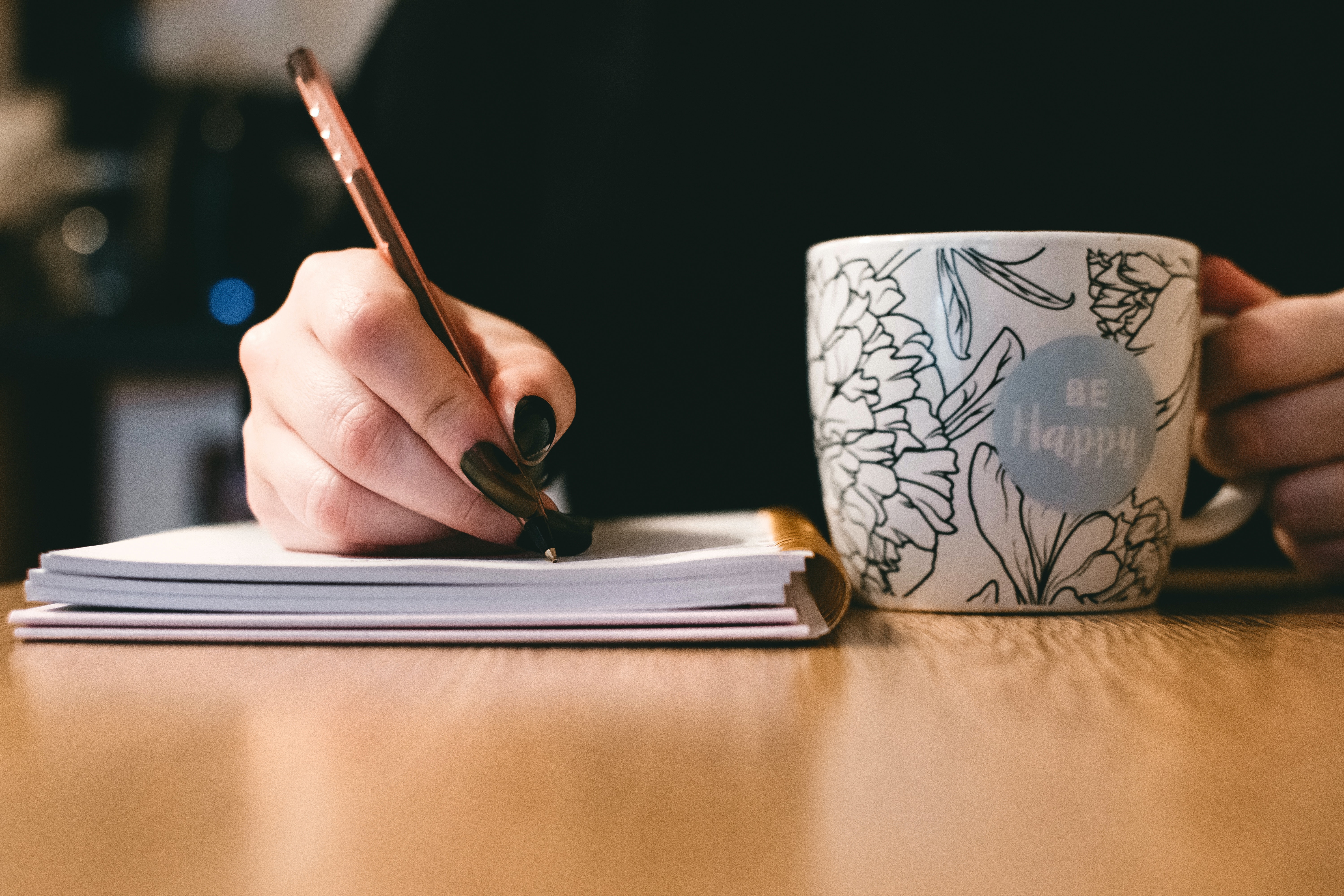 Person writes in a note book with a a hot mug drink