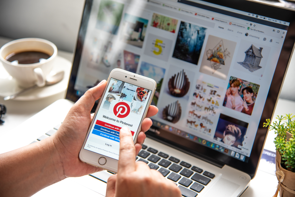 Person logs into Pinterest mobile app on their smart phone with Pinterest home page open on the desktop in the background