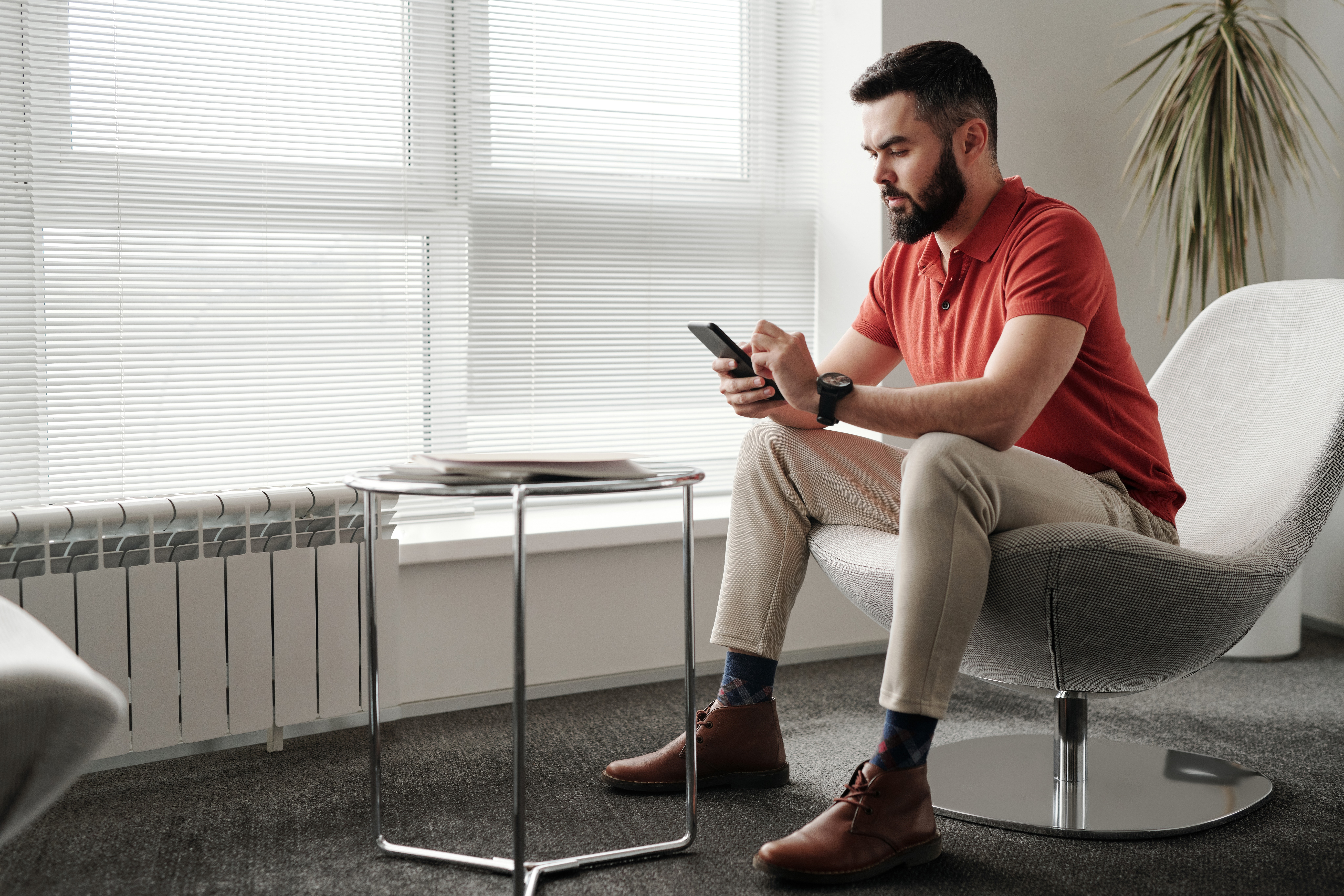 Man in red polo sits in a modern office chair, reading his phone