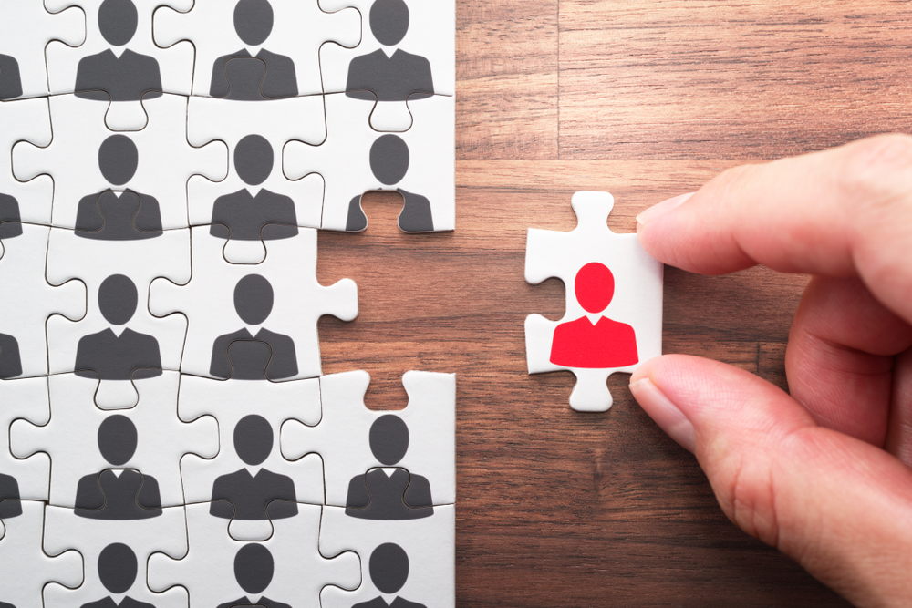 Hand Holding a puzzle piece up to a larger audience of customer puzzle pieces