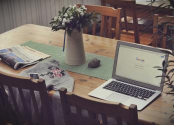 Work from home workspace: laptop, newspaper, phone, and jacket laid on kitchen table