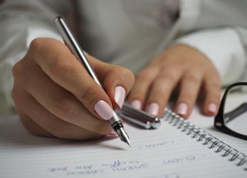 Hand with painted nails writing in planner with glass to the side