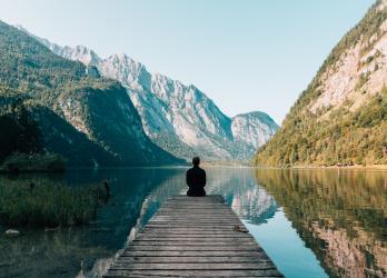 Person sits on end of dock surrounded by mountains 