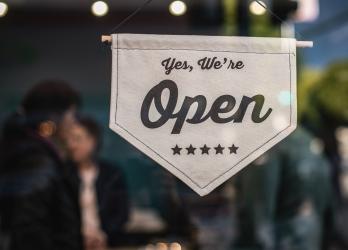 Store window with shallow focus on flag that says, "Yes, we're open."