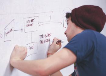 Man wearing a beanie create flow chart on white board