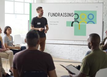 Man presents to group of people while standing in front of a board saying "Fundraising"