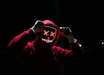 Person in a red hoodie with a neon skull face mask in a darkened room