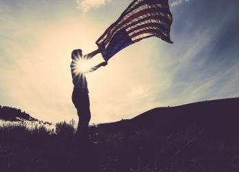 Backlit person waving out a U.S. Flag.