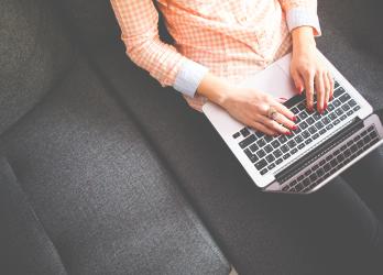 Person in Smart Casual clothes sits on a grey sofa, using their laptop