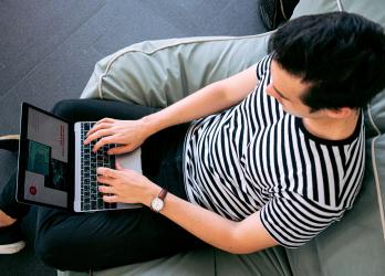 Top down view of a man in a black and white shirt using a laptop