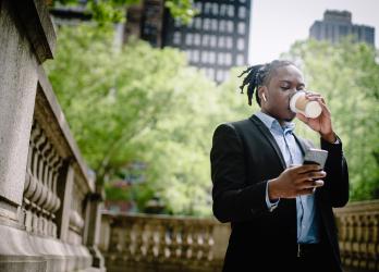 Young professional sips a to-go coffee mug and looks this mobile device