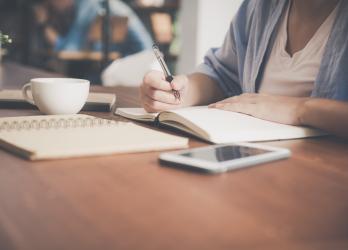 Person writing at a desk with multiple notebooks