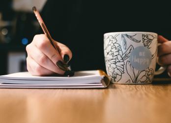 Person writes in a note book with a a hot mug drink