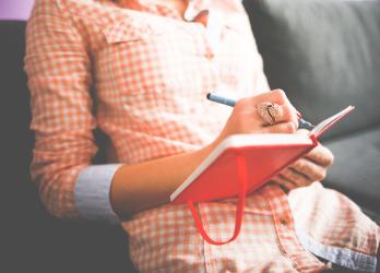 Person in orange plaid shirt writes in a red journal