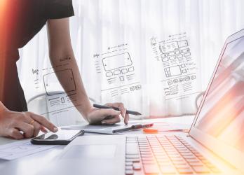 Web designer works on a computer with web design wire frame drawing super-imposed over them