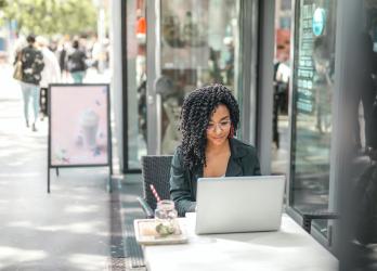 Young black woman works on laptop outside of city coffee shop 