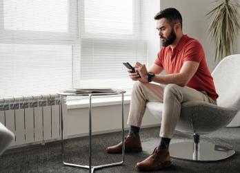 Man in red polo sits in a modern office chair, reading his phone