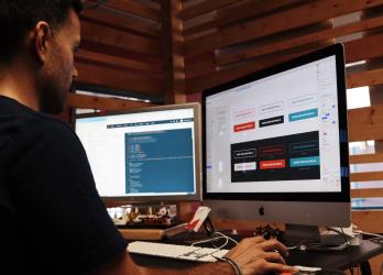 Man working on a computer with two monitors editing web design and development tools 