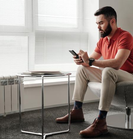 Man in red polo sits in a modern office chair, reading his phone